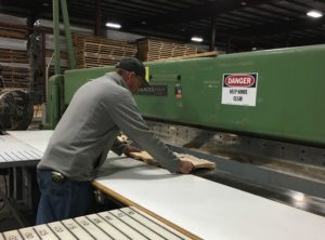 A worker pushes a bundle of wood veneer on the work table attached to the clipper machine to be clipped to have a more clean edge.